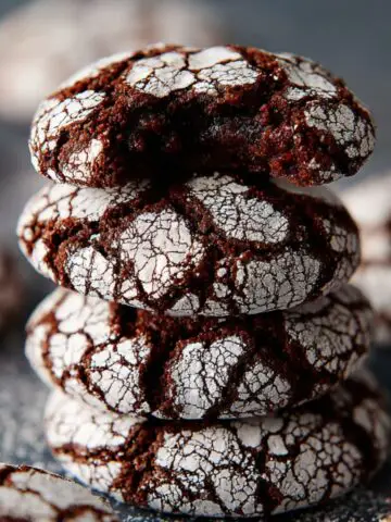 Stack of homemade chocolate crinkle cookies with cracked powdered sugar tops, showing their soft, fudgy centers and rich texture.