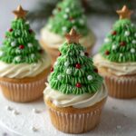Homemade Christmas tree cupcakes topped with green buttercream trees, red and white candy ornaments, and gold star toppers.