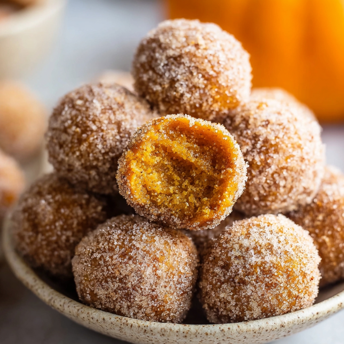 Cinnamon Sugar Pumpkin Donut Holes piled together, with one donut hole on top showing a soft, moist pumpkin interior.