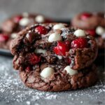 Easy Black Forest Cookies Recipe with gooey melted chocolate, bright red cherries, and white chocolate chunks, sitting on a dark surface dusted lightly with powdered sugar.