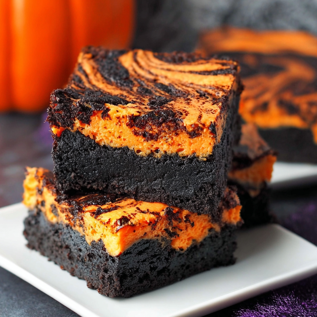 Easy Halloween Swirl Cream Cheese Brownies stacked on a white plate, showing rich dark chocolate layers and vibrant orange cheesecake swirls with a soft, fudgy texture.