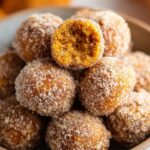 Homemade Cinnamon Sugar Pumpkin Donut Holes piled together, with one donut hole on top showing a soft, moist pumpkin interior.
