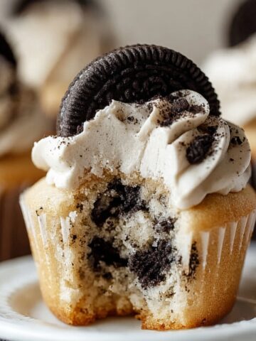 Homemade Cookies and Cream Cupcakes with vanilla frosting and a whole Oreo on top, showing a soft bite revealing crushed cookies inside.