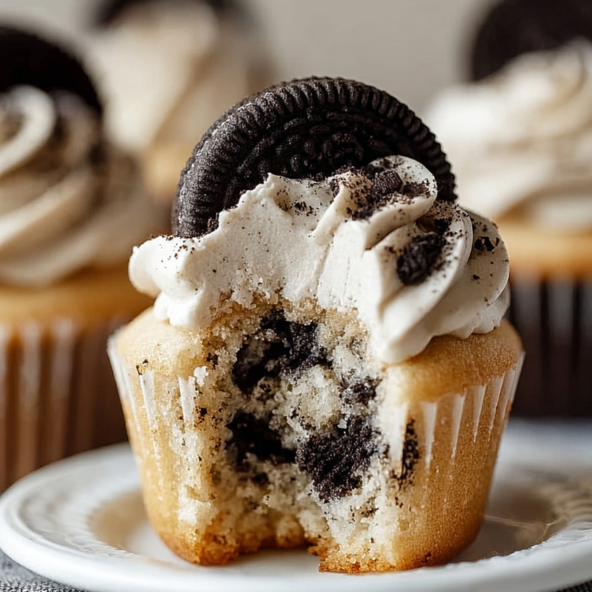 Homemade Cookies and Cream Cupcakes with vanilla frosting and a whole Oreo on top, showing a soft bite revealing crushed cookies inside.