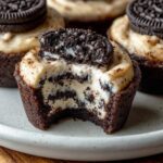 Homemade Oreo Cheesecake Cookie Cups with creamy cheesecake filling, Oreo layers, and a bite taken out on a white plate.