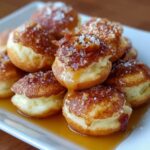 Homemade pancake poppers stacked on a white plate, golden-brown and fluffy with crisp edges, drizzled in warm maple syrup and sprinkled with coarse sugar for a rustic, cozy look.