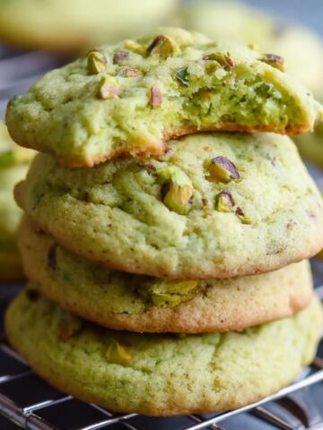 Homemade Pistachio Pudding Cookies on a cooling rack, topped with chopped pistachios and a soft chewy green center visible from a half-eaten cookie.