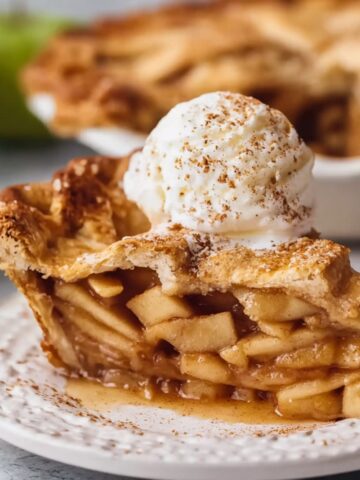 Homemade Vegan Apple Pie topped with a scoop of vanilla ice cream and cinnamon on a white plate.