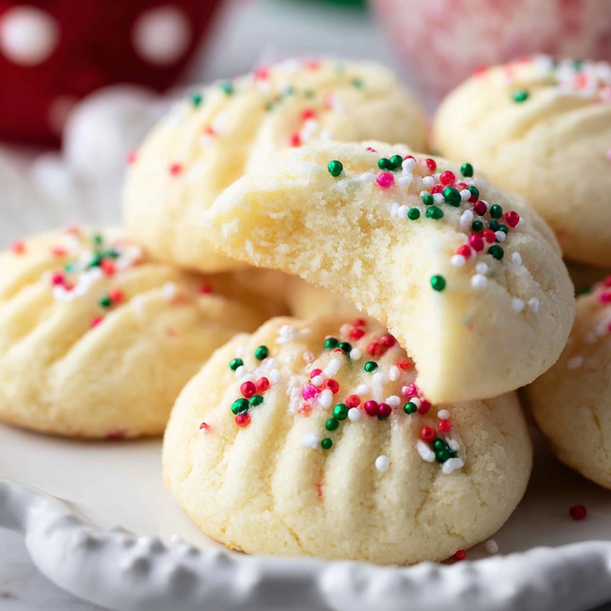 Homemade Whipped Shortbread Cookies topped with red, green, and white sprinkles, with one cookie showing a bite taken out to reveal its soft, crumbly texture.