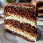 A homemade slice of Italian Love Cake with moist chocolate layers and creamy ricotta filling, shown close up on a white plate in warm natural sunlight.