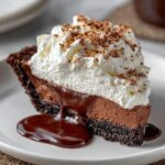Mississippi Mud Pie with a dark cookie crust, creamy chocolate filling, whipped cream topping, and chocolate sauce dripping onto a white plate.