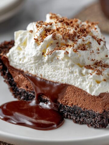 Mississippi Mud Pie with a dark cookie crust, creamy chocolate filling, whipped cream topping, and chocolate sauce dripping onto a white plate.