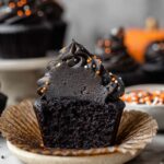 Black Velvet Cupcakes with black buttercream frosting and orange, white, and black sprinkles on a marble surface.