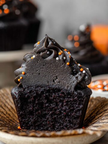Black Velvet Cupcakes with black buttercream frosting and orange, white, and black sprinkles on a marble surface.