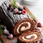A beautifully decorated Bûche De Noël, dusted with powdered sugar and topped with frosted berries and rosemary.