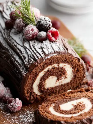 A beautifully decorated Bûche De Noël, dusted with powdered sugar and topped with frosted berries and rosemary.