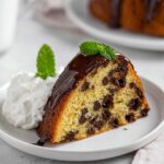 Chocolate Chip Bundt Cake Recipe topped with glossy chocolate ganache, mint leaves, and whipped cream on a plate.