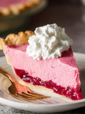 A slice of cranberry custard pie with a layer of whipped cream on top, showing the vibrant pink filling and cranberry layer.