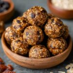 A bowl filled with homemade energy bites, perfectly shaped into small, round balls with a mixture of oats and chocolate chips. The energy bites appear homemade and rustic, with a natural texture and slight imperfections, surrounded by ingredients like oats and dried fruits.