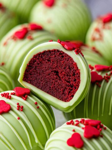 Best Grinch Oreo Balls Recipe 2 Grinch Oreo Balls with red velvet inside, decorated with red heart sprinkles and a swirl pattern.