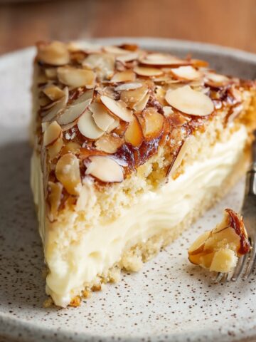 Homemade Bee Sting Cake with creamy filling and caramelized sliced almonds sits on a speckled plate beside a fork.