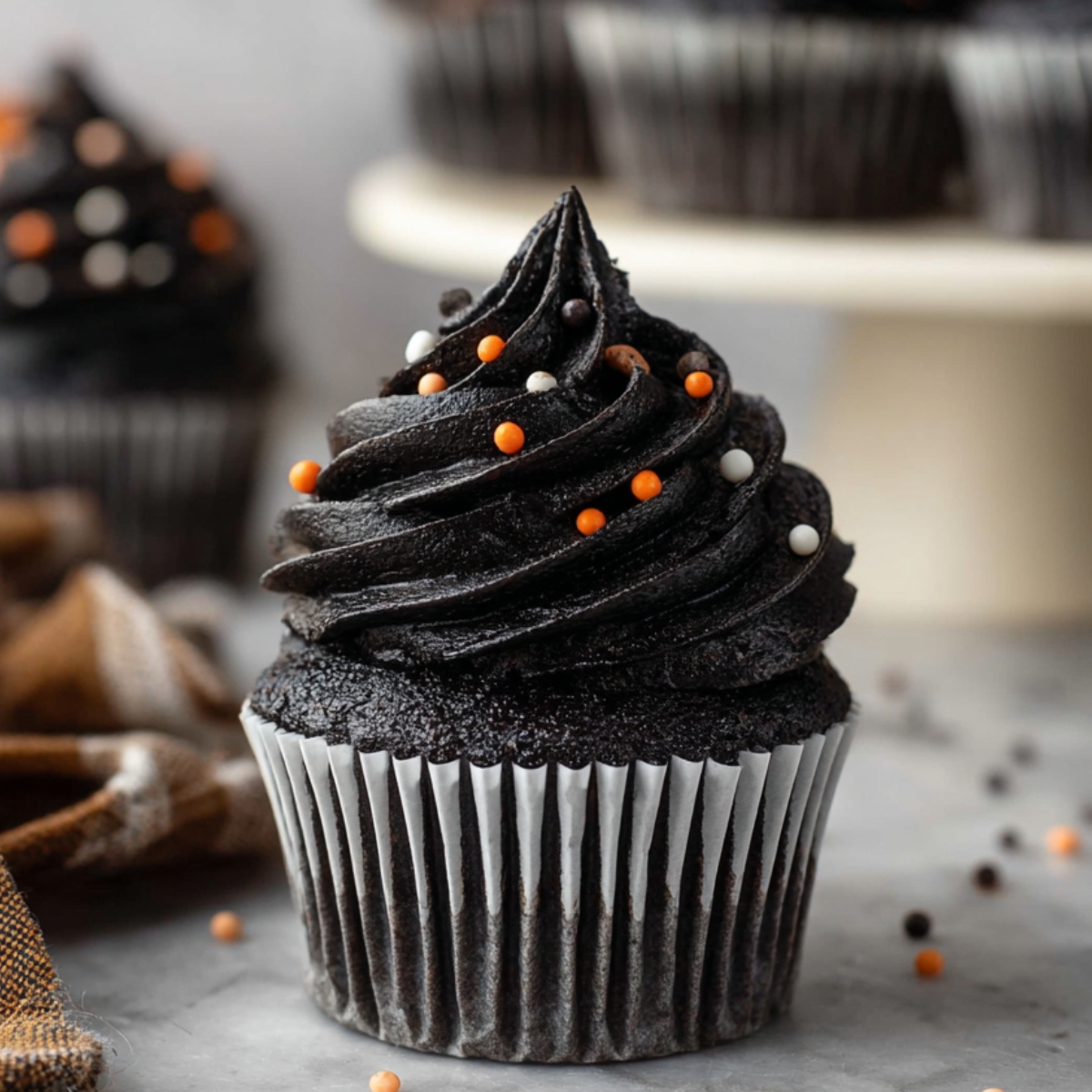 Black Velvet Cupcakes 12 Homemade black velvet cupcake sliced in half, showing its moist dark crumb and black buttercream frosting with orange, white, and black sprinkles.