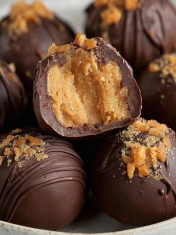 Homemade Butterfinger Balls topped with crushed candy, with one truffle bitten open to show its soft peanut butter filling.