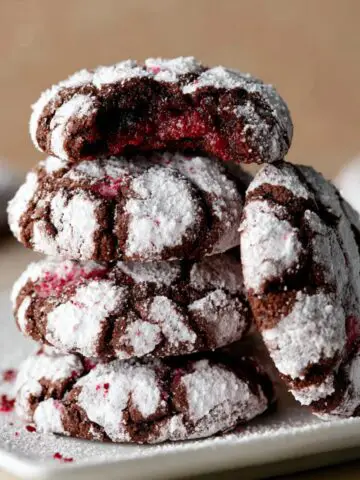 Homemade Chocolate Raspberry Crinkle Cookies dusted with powdered sugar, with one cookie bitten into, revealing a red raspberry filling.