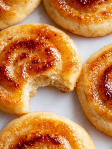 Homemade Creme Brûlée Cookies with a caramelized swirl, one with a bite taken out to reveal its soft interior.