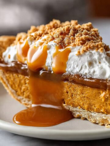 Homemade Pumpkin Caramel Pie topped with whipped cream and cookie crumbs, with caramel sauce dripping down the sides onto the plate.