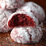 Homemade Red Velvet Snowball Cookies dusted with powdered sugar, one cookie broken open to show the soft red interior.