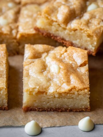 Homemade White Chocolate Brownies, cut into squares with a golden, cracked top and scattered white chocolate chips.