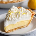 A slice of lemon cream pie with a creamy filling, topped with whipped cream and lemon zest.