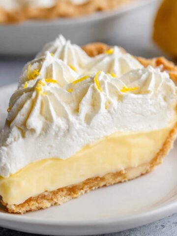A slice of lemon cream pie with a creamy filling, topped with whipped cream and lemon zest.