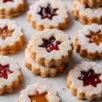 Close-up of Linzer cookies with star-shaped cutouts, filled with raspberry and apricot jam, dusted with powdered sugar.