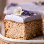 London Fog Cake topped with lavender-colored frosting, garnished with a sprig of lavender and a small white flower.