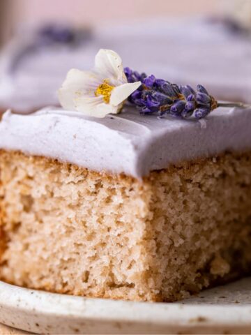 London Fog Cake topped with lavender-colored frosting, garnished with a sprig of lavender and a small white flower.