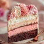 Slice of homemade Neapolitan cake with chocolate, strawberry, and vanilla layers, topped with pink and white buttercream swirls on a plate.