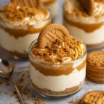 No-Bake Biscoff Cheesecake Cups topped with whipped cream, caramel sauce, crushed Biscoff cookies, and a whole Biscoff biscuit.