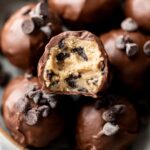 Close-up of chocolate-coated Cookie Dough Truffles, with one truffle halved to reveal the gooey cookie dough and chocolate chips inside.