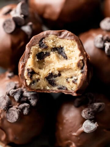 Close-up of chocolate-coated Cookie Dough Truffles, with one truffle halved to reveal the gooey cookie dough and chocolate chips inside.