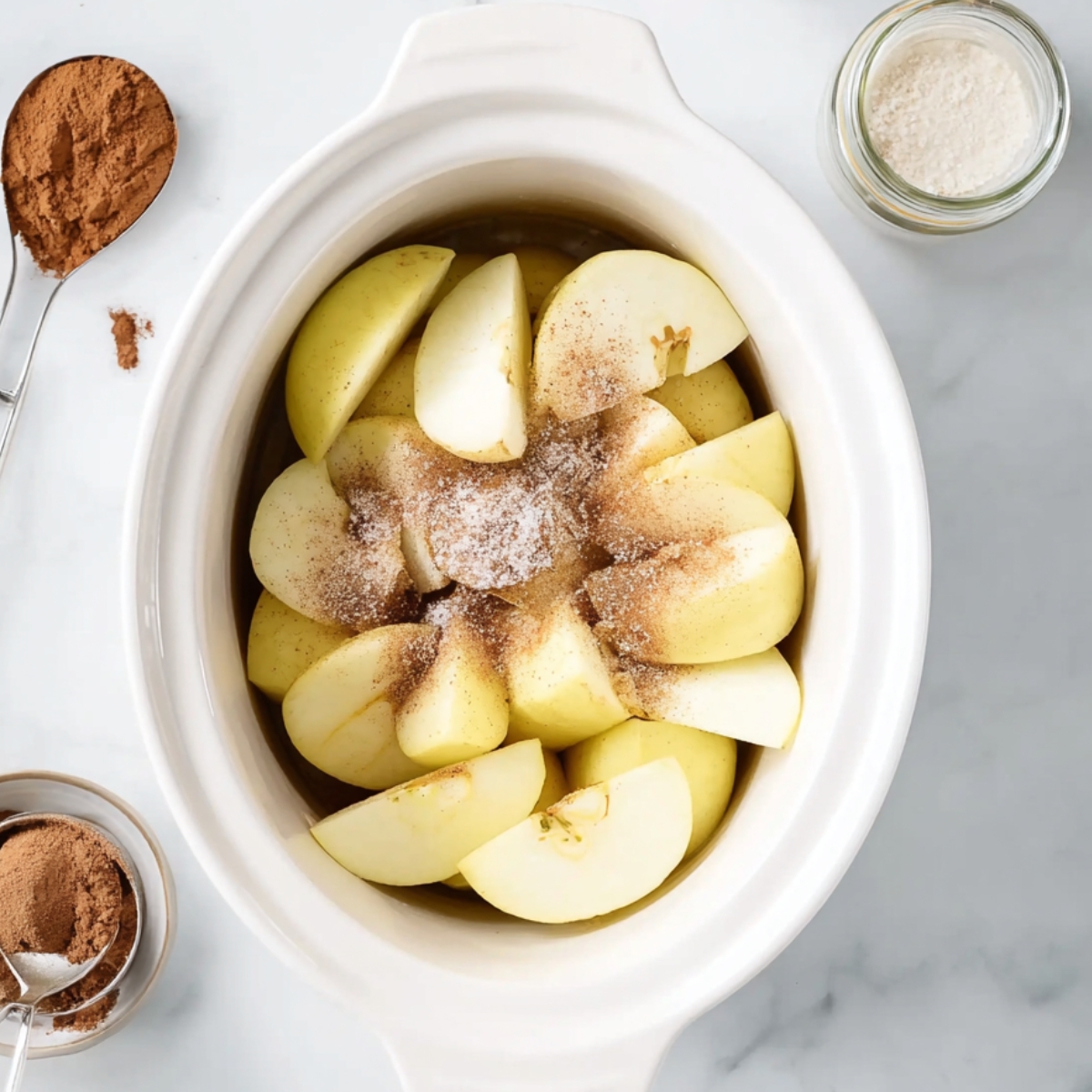 Quartered apples in a slow cooker sprinkled with sugar and cinnamon, ready to cook into homemade crockpot applesauce.