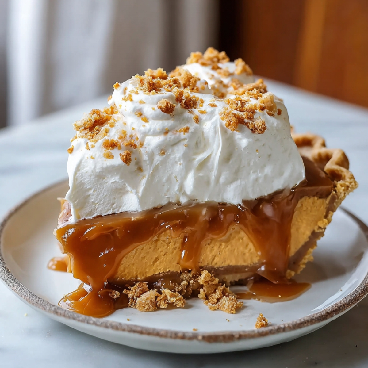 A slice of homemade pumpkin caramel pie topped with whipped cream, crumbled cookie topping, and thick caramel sauce dripping down the sides onto a plate.