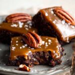 Salted Caramel Turtle Brownies with a bite taken out, topped with a pecan and sea salt flakes.