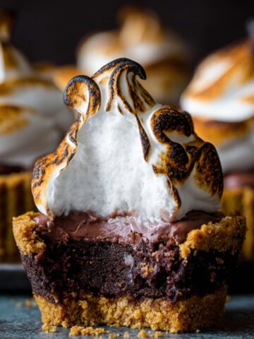 A smores brownie cupcakes with a golden graham cracker crust, gooey chocolate center, and a perfectly toasted marshmallow topping.