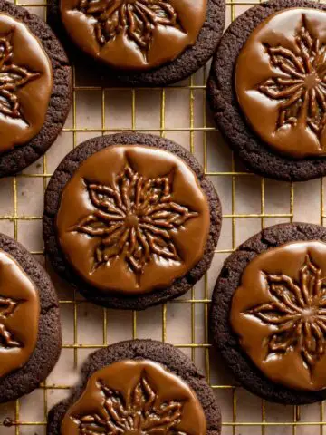 Stamped Chocolate Espresso Cookies 3 Stamped Chocolate Espresso Cookies topped with glossy espresso glaze and stamped floral designs, cooling on a gold wire rack.