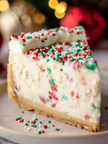 Sugar Cookie Cheesecake 1 Slice of Sugar Cookie Cheesecake topped with red, green, and white sprinkles, with a festive background.