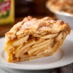 Slice of Apple Cheddar Pie on a white plate showing layered apple filling and flaky golden crust