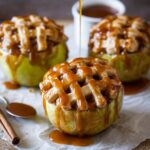 Apple Pie Baked Apples with a golden lattice crust, topped with a generous drizzle of caramel sauce, ready to be served as a warm, indulgent dessert.