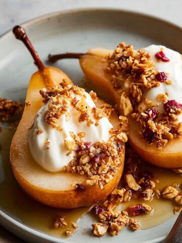 Easy Baked Pears Recipe | 4 Ingredients, 30 Minutes 5 Two baked pears topped with yogurt, granola, and dried cranberries, served on a light plate with a drizzle of syrup.